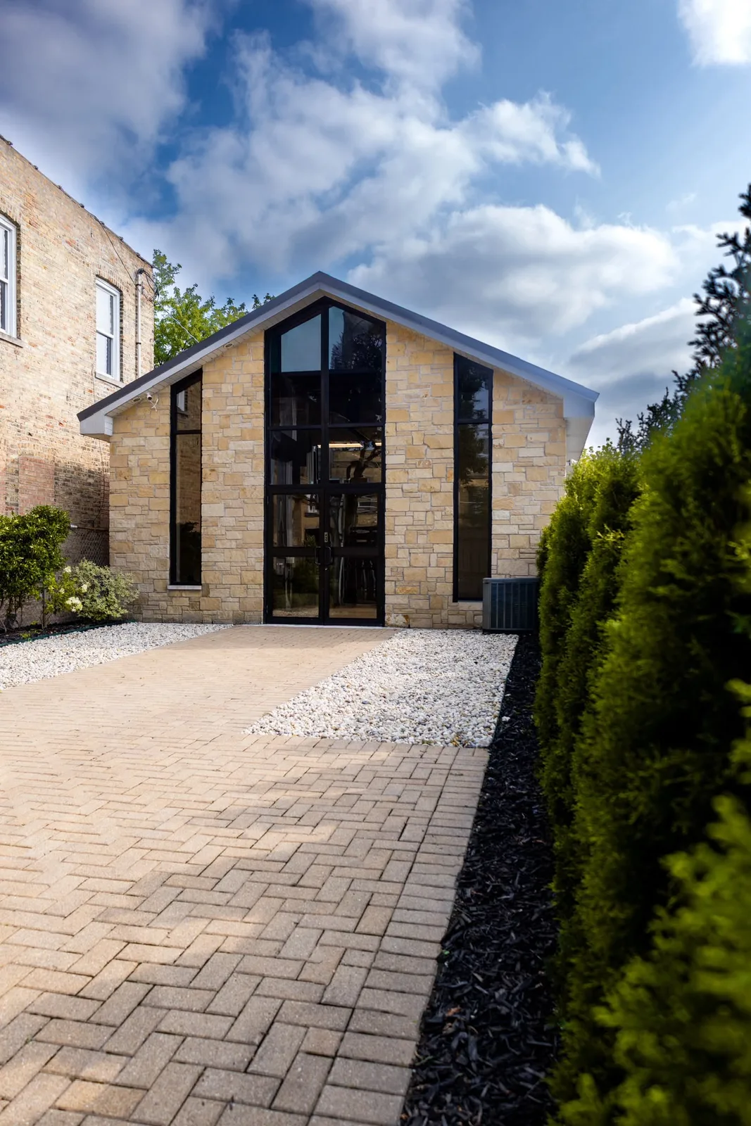 The brick-path entrance to MARPA Studio, a gabled stone building with tall black windows