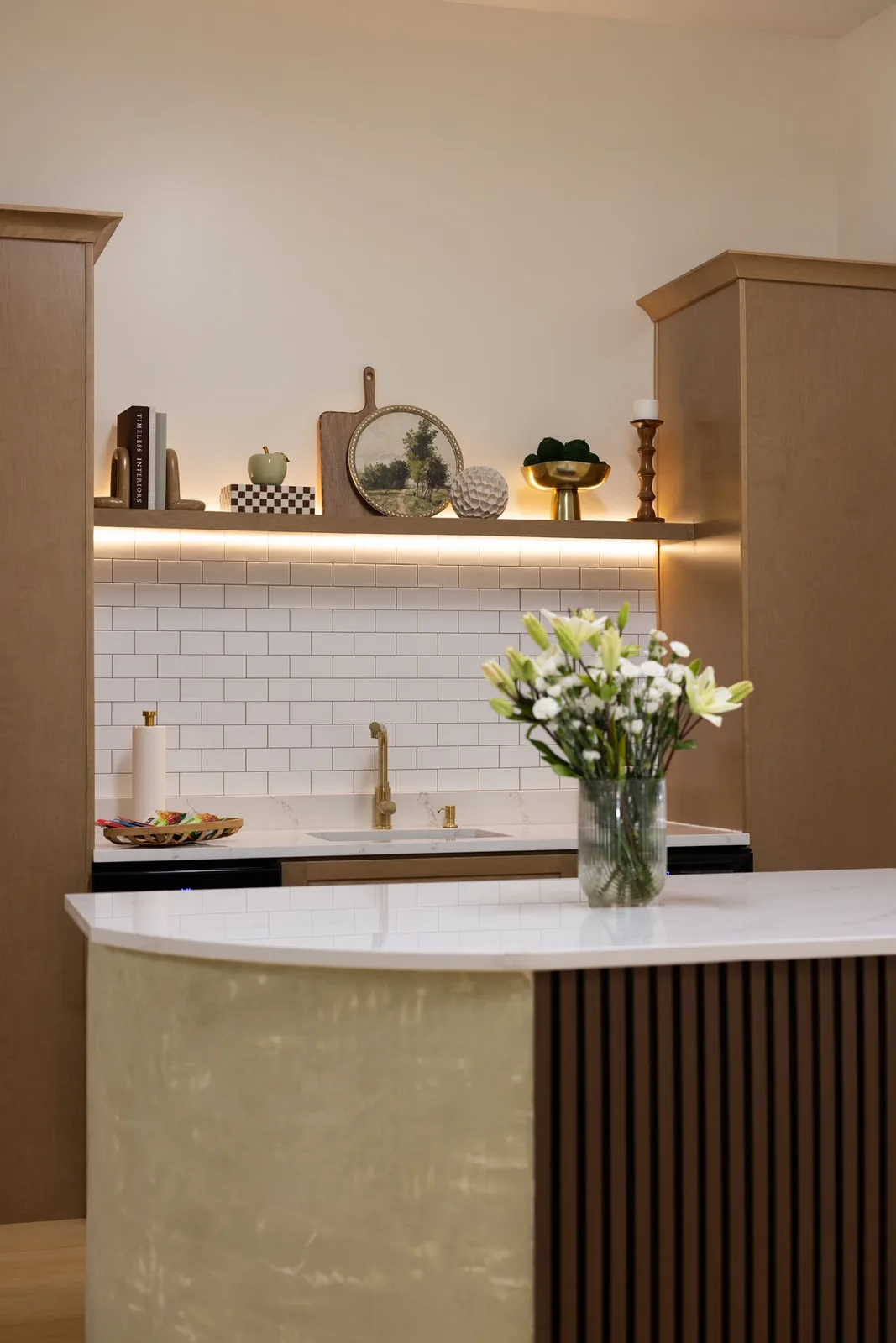 Kitchenette with a fluted island, white tile and fresh white flowers