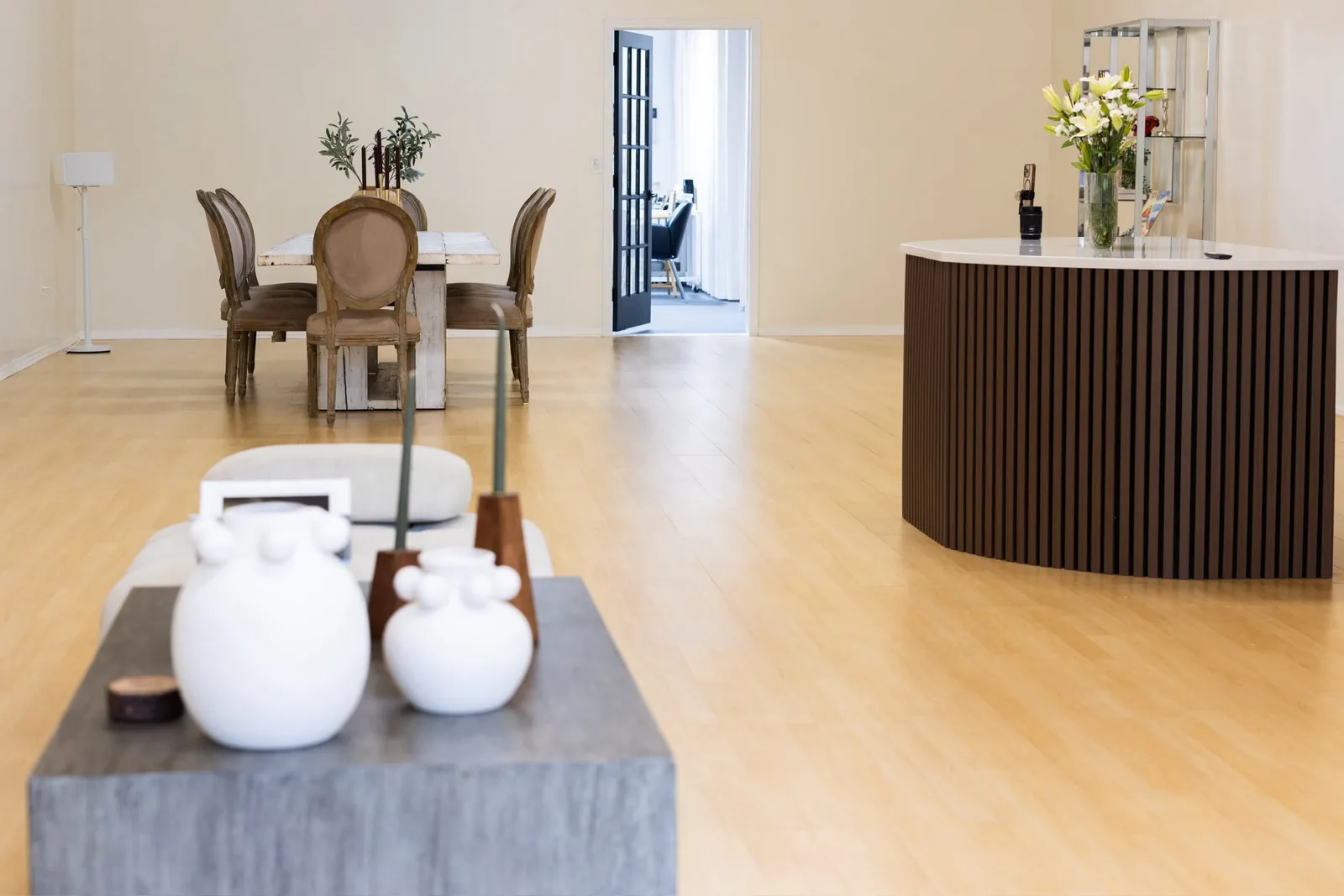 Open room with light wood floors, a dining table and a fluted kitchenette island