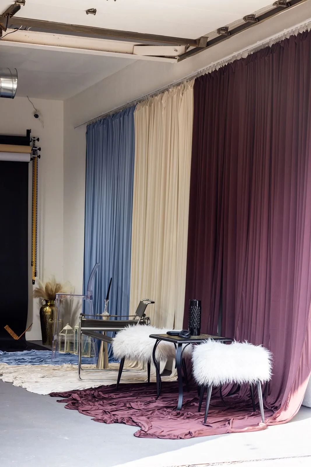 Photo studio with blue, beige and plum curtains, a rug and white stools