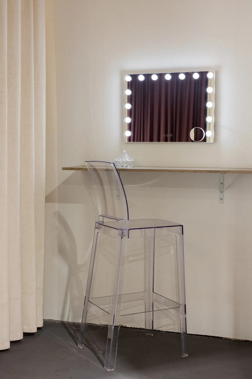 Dressing area with a lit vanity mirror and a clear stool